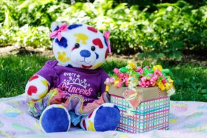 Colorful teddy bear with a wrapped gift box outdoors on a sunny day.