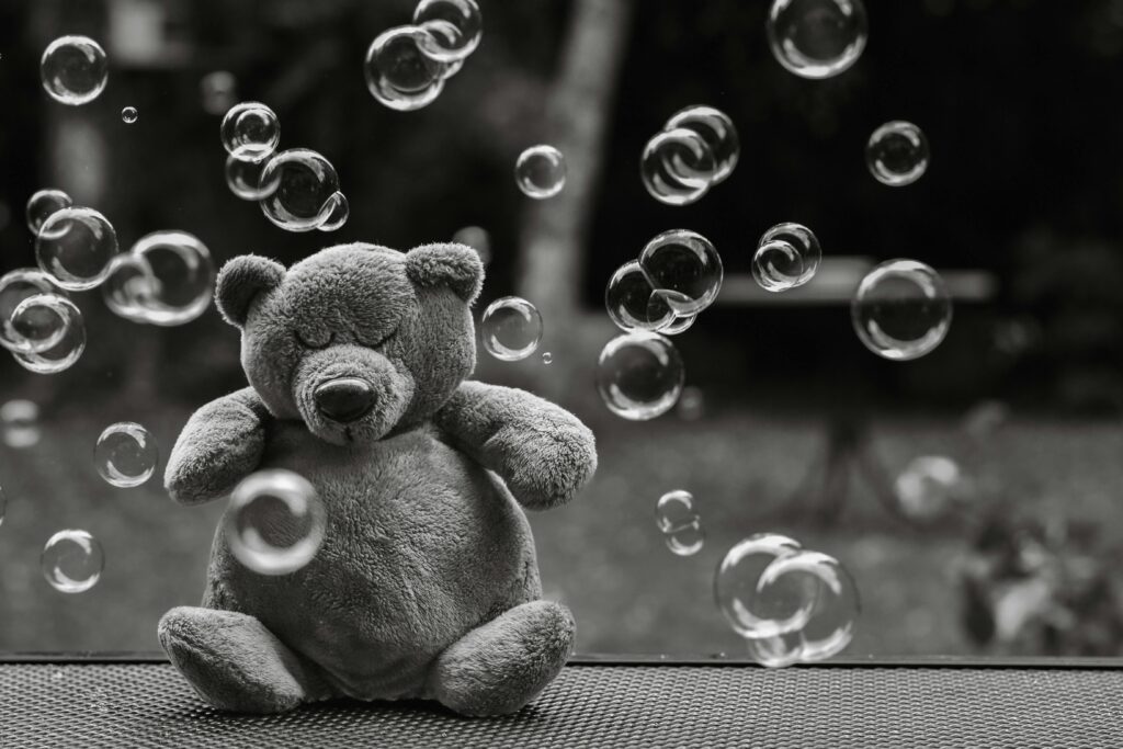 A soft teddy bear surrounded by bubbles in a serene outdoor setting, captured in black and white.